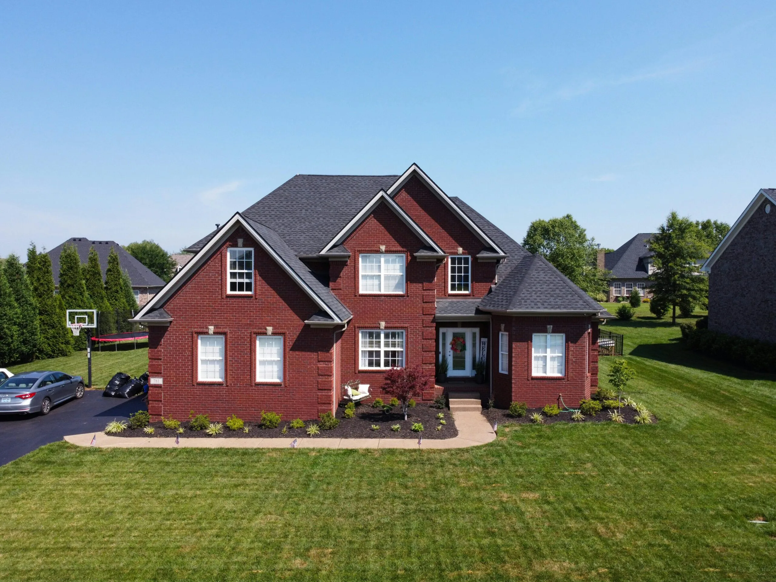 A beautiful brick house with manicured lawn in a suburban neighborhood on a sunny day.